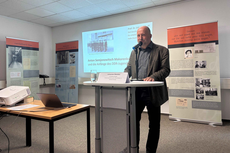 Mann am Rednerpult im Hintergrund Vortragspräsentation und Ausstellungsrollups