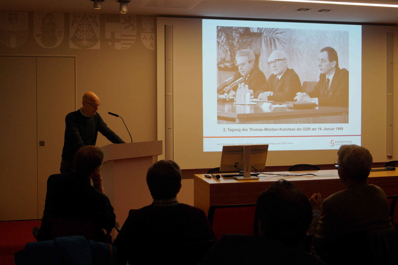 Dr. Jan Scheunemann am Rednerpult, zu seiner Rechten die Power-Point-Präsentation mit Erich Honecker während einer Pressekonferenz zur Tagung des Thomas-Müntzer-Komitees der DDR am 19. Januar 1989