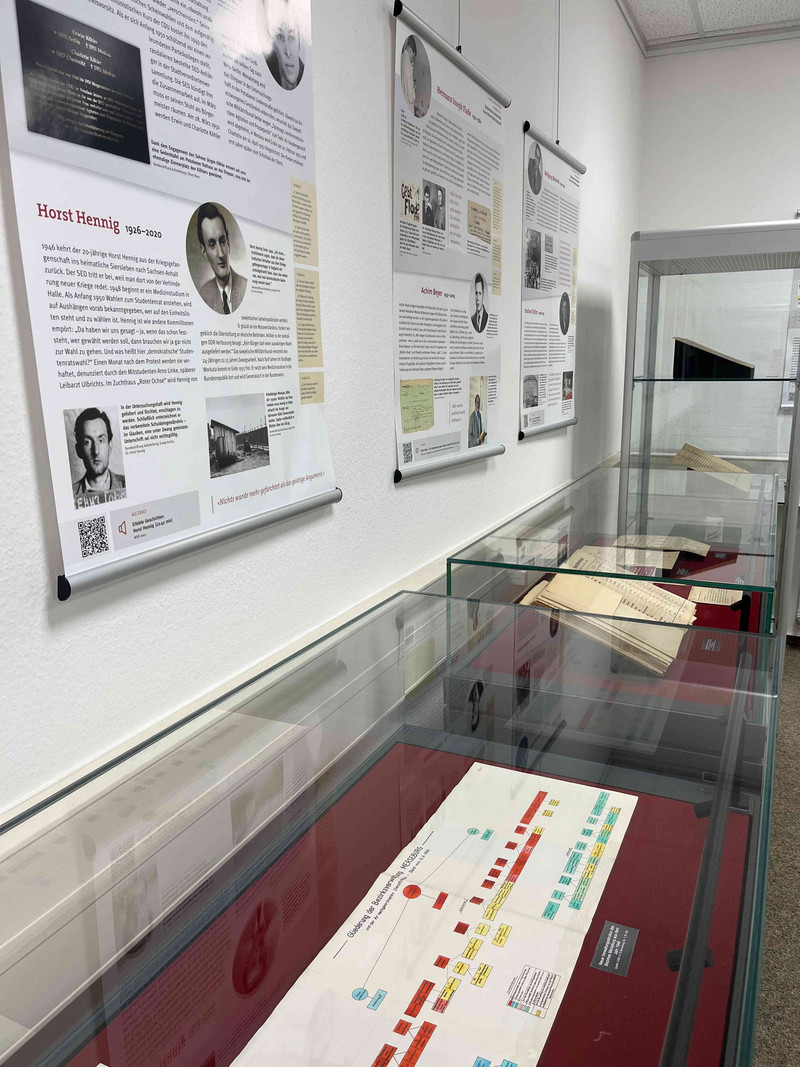 Auf der linken Seite hängen die Plakate der Ausstellung, davor stehen Tischvitrinen mit Archivalien zur Nachkriegssituation im Bezirk Merseburg der Jahre 1945 bis 1946 aus den Beständen des Landesarchivs Sachsen-Anhalt
